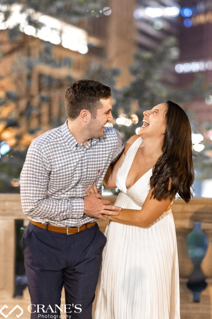 A Chicago wedding photographer freezes a moment of pure joy in a photograph. The nighttime image captures an engaged couple, bathed in the warm glow of Chicago's downtown lights, lost in a fit of laughter