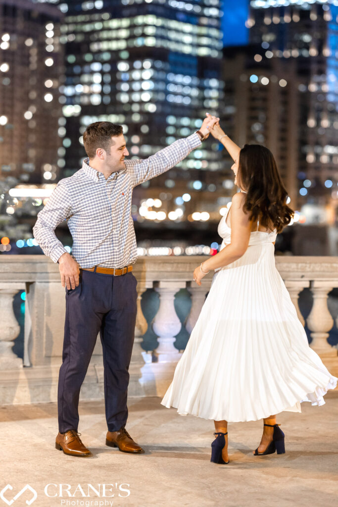 Nighttime engagement photo in downtown Chicago capturing a candid moment of the couple twirling. The woman is wearing a white dress.