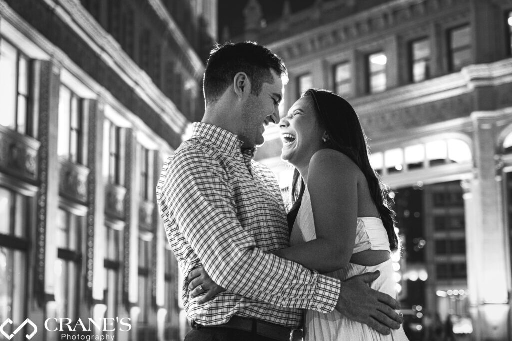 An engaged couple laughing during their nighttime engagement session in downtown Chicago.