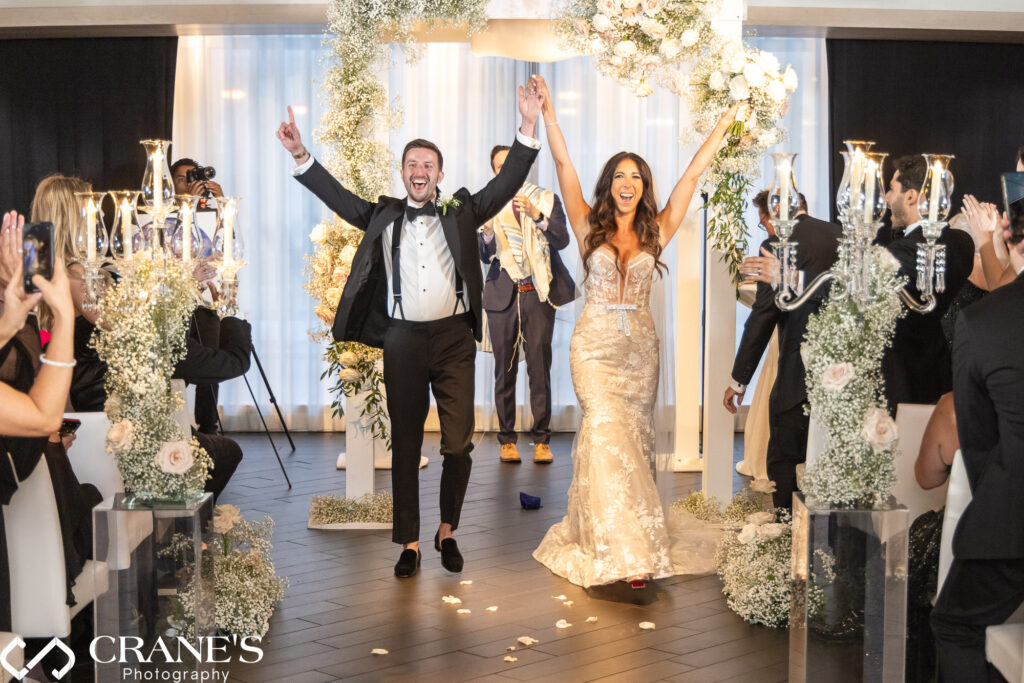 At their wedding ceremony at RPM Events, the bride and groom cheer with their hands in the air as they are pronounced husband and wife for the first time. The moment captures their joyous celebration and excitement of the newlyweds.