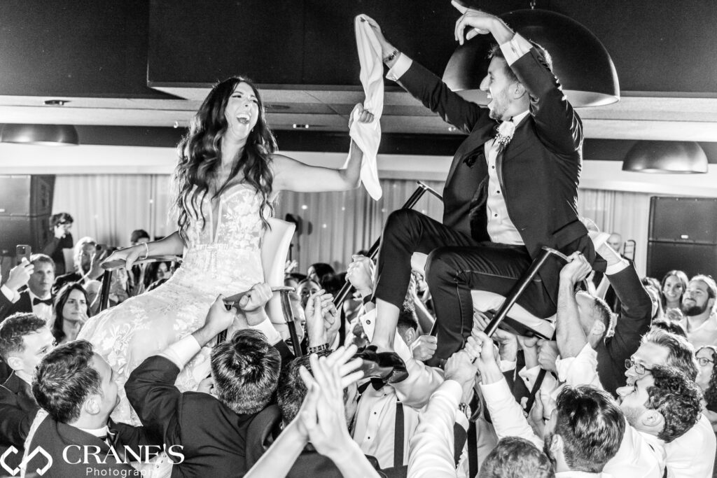 A fun-filled moment at a black-tie wedding reception at RPM Events: the bride and groom are joyfully lifted in chairs during the Hora dance, a symbol of their new life together.