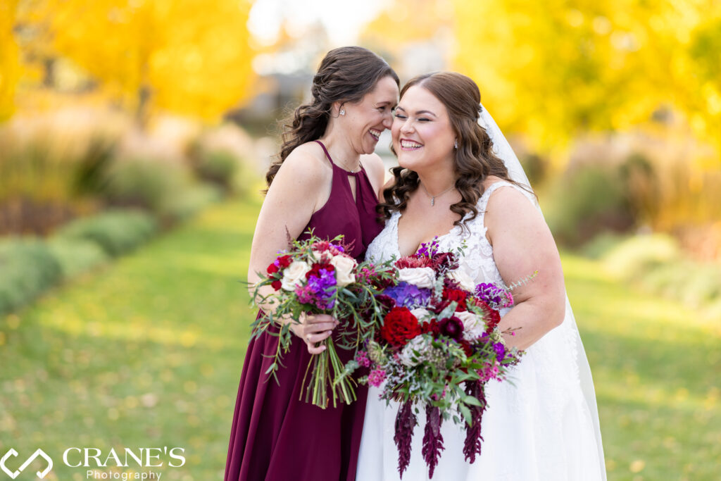 Bride laughing with her bridesmaid at their wedding at the Morton Arboretum, sharing a joyful moment amidst the beautiful outdoor setting.