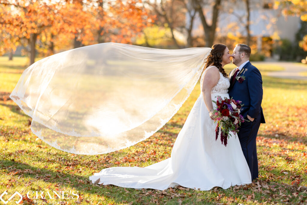 Bride's veil floating gracefully in the air around her as the kiss, capturing a moment of elegance and movement during her wedding at the Morton Arboretum.