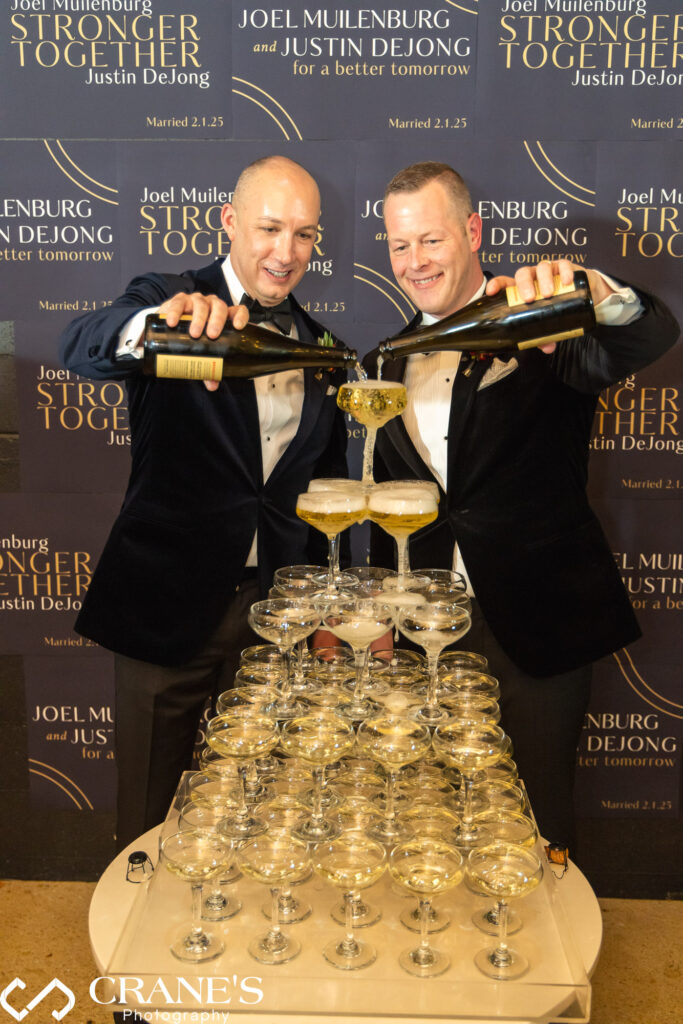 Wedding photo of Joel Muilenburg and Justin DeJong with "Stronger Together" text overlay, pouring champagne into a tower at their Chicago Winery reception. Photo by Crane's Photography.