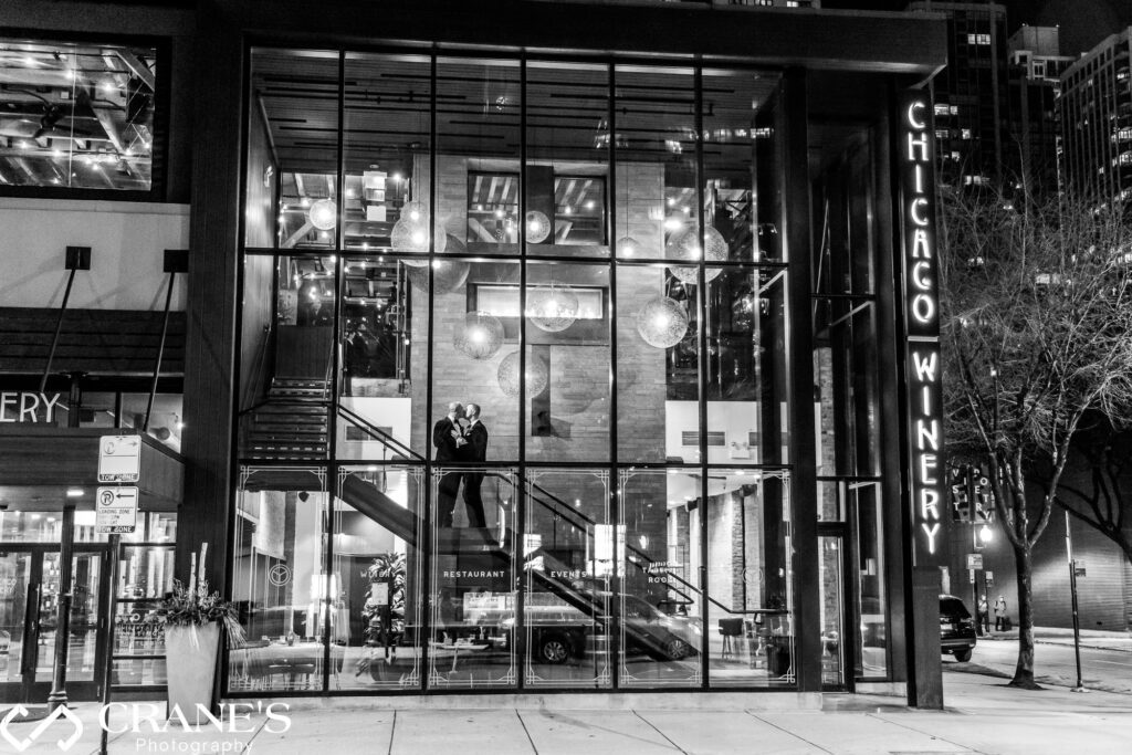 Night wedding photo taken from the street showing a gay couple kissing on the exterior stairs of the Chicago Winery.