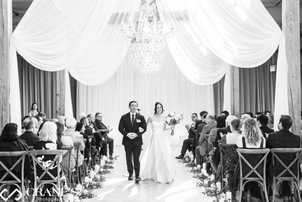 Bride and groom walk down the aisle after their wedding ceremony at The Skyline Loft beneath grand chandeliers and flowing white drapery, surrounded by seated guests