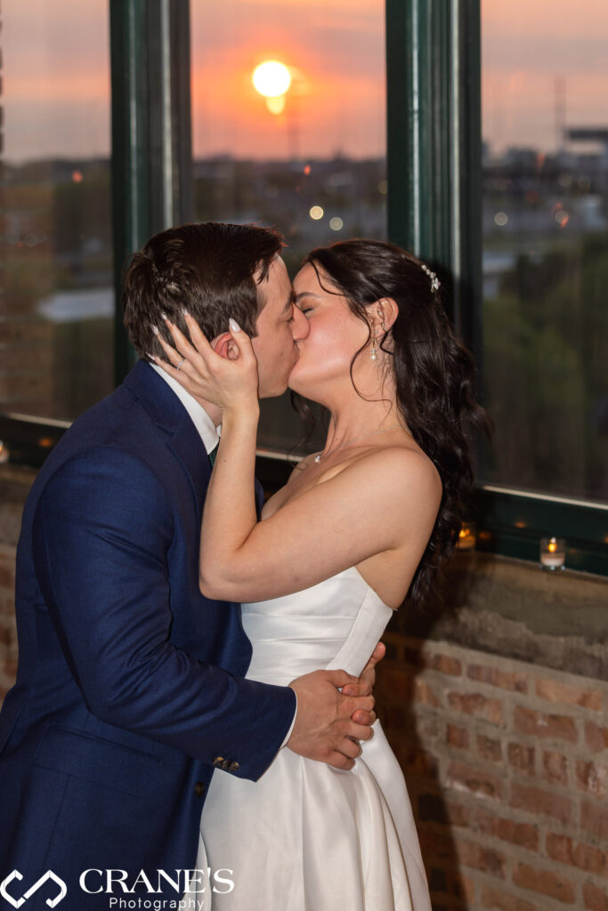 Bride and groom share a romantic kiss at sunset with the city skyline glowing in the background, viewed from the Skyline Loft at Bridgeport Art Center on their wedding day.